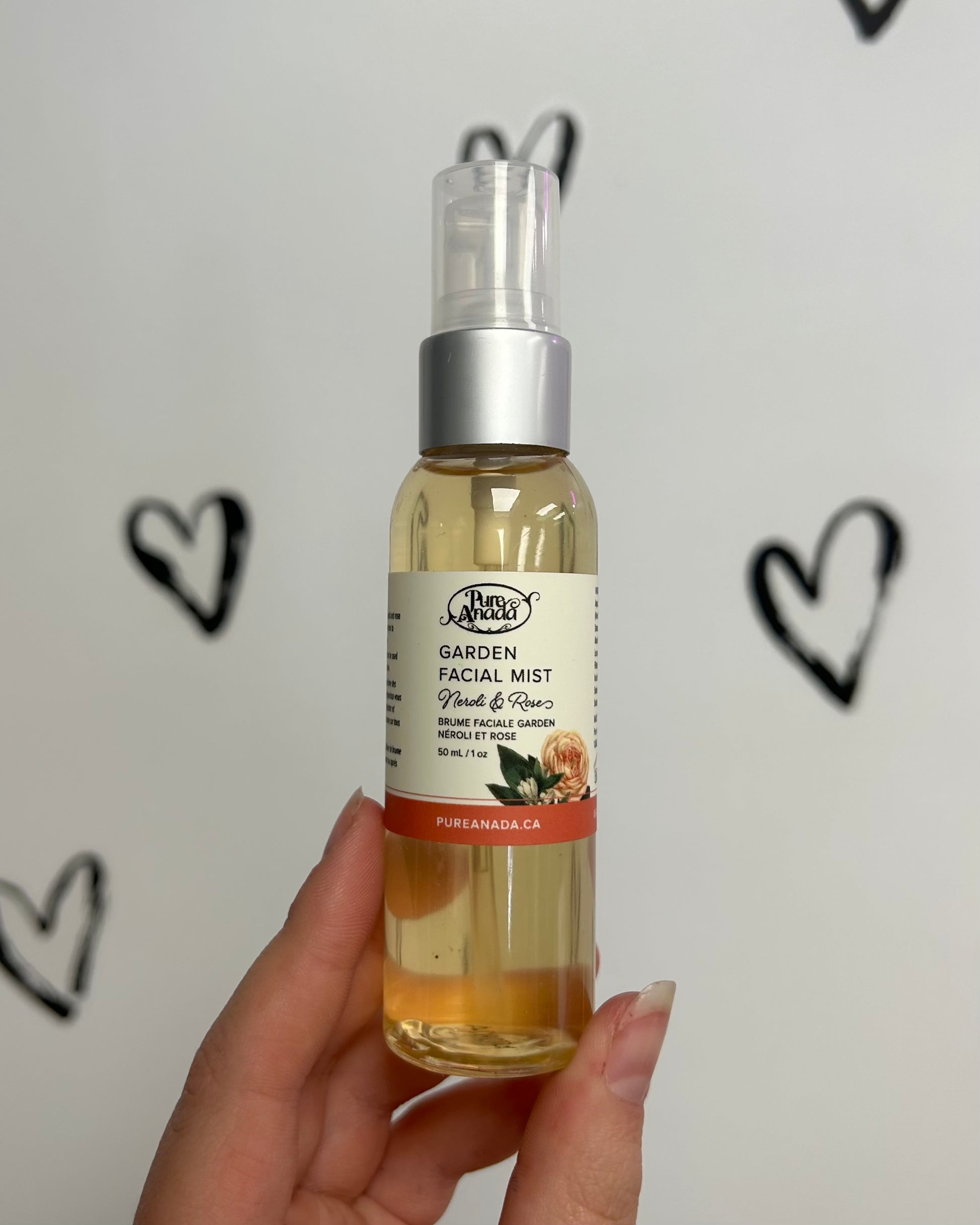 Hand holding a bottle of Garden Facial Mist with a white background featuring black heart shapes.