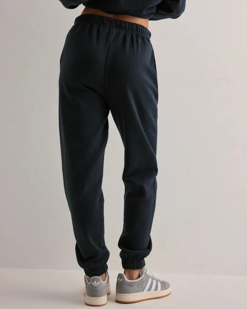 Person wearing black sweatpants and gray sneakers on a plain background