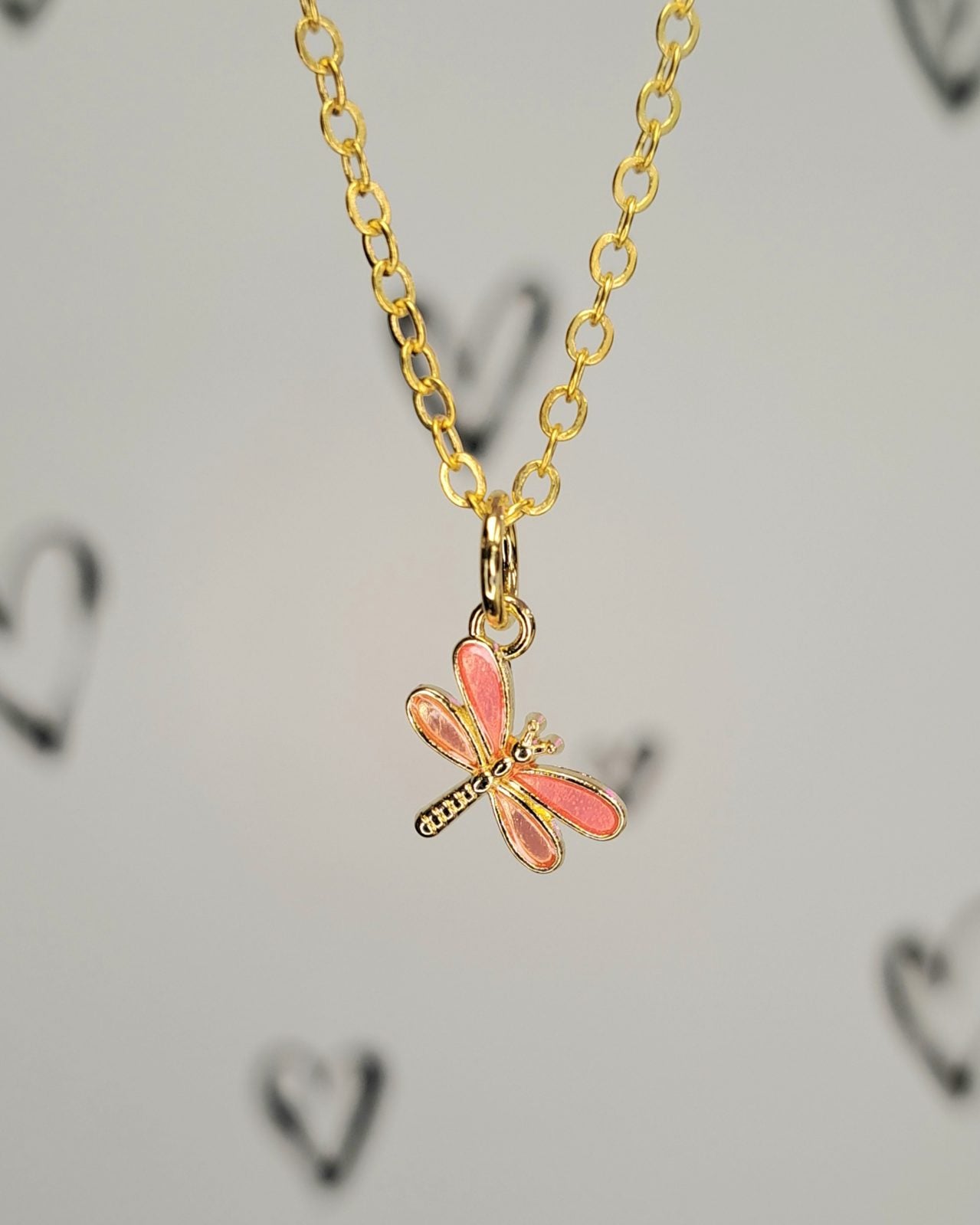 Gold necklace with a pink dragonfly pendant on a light gray background