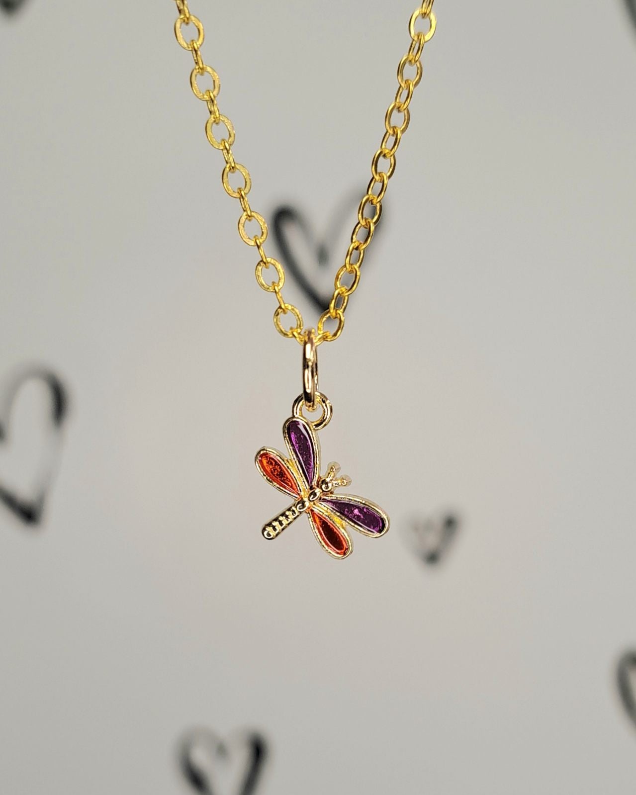 Gold necklace with a dragonfly pendant on a light gray background