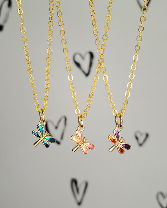 Three colorful butterfly necklaces on gold chains against a gray background with heart designs.